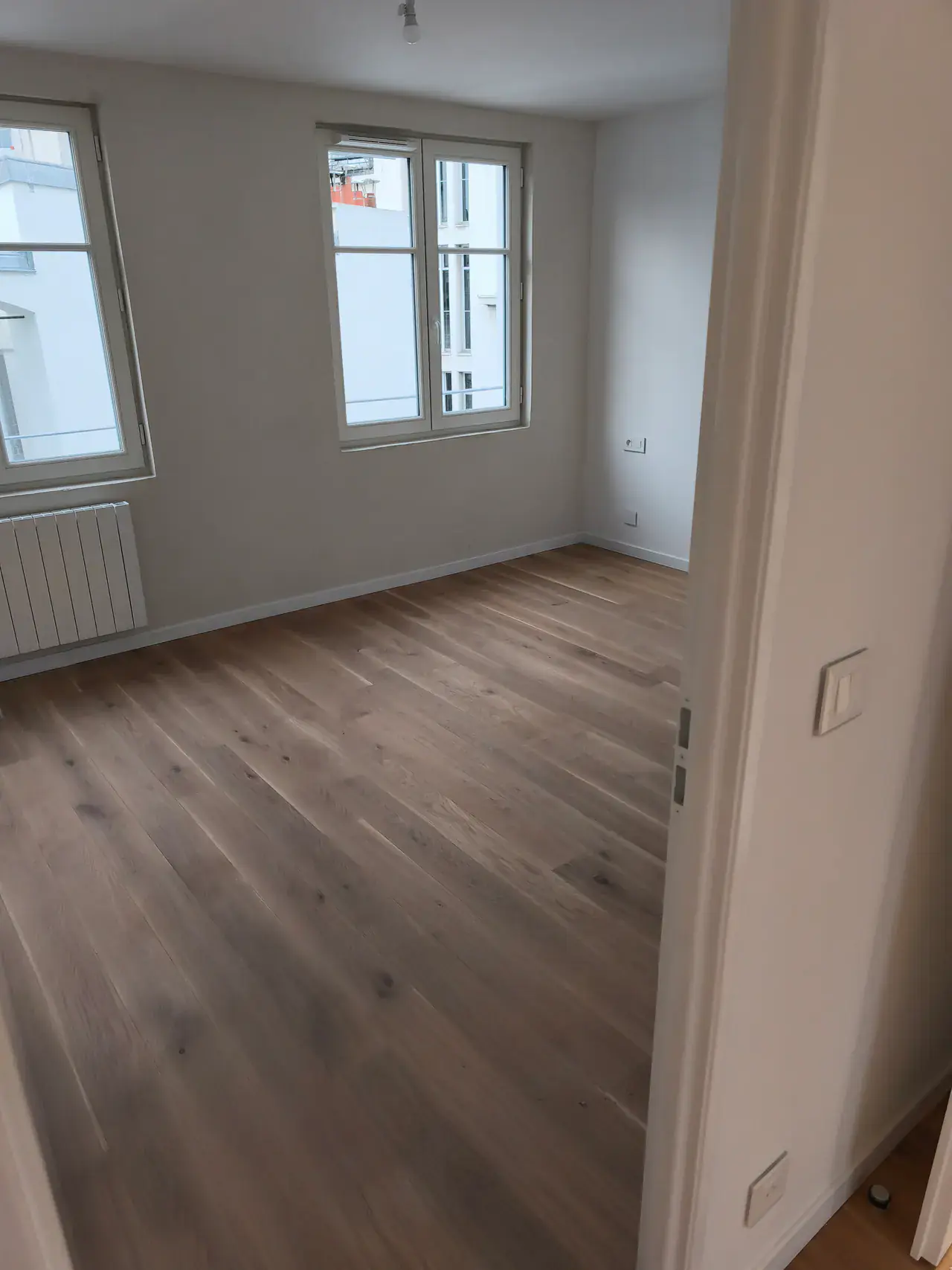Chambre livrée avec parquet clair, murs clairs et deux fenêtres
