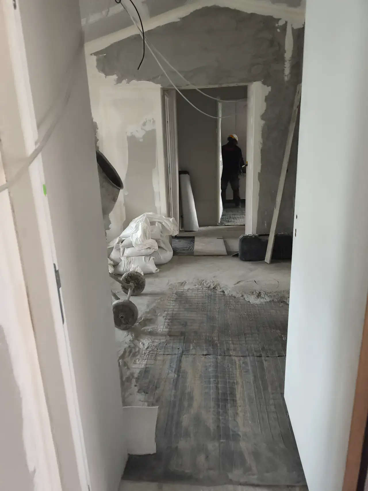 Couloir de logement en chantier, planchers dégagés et cloisons montées, avec un compagnon au travail