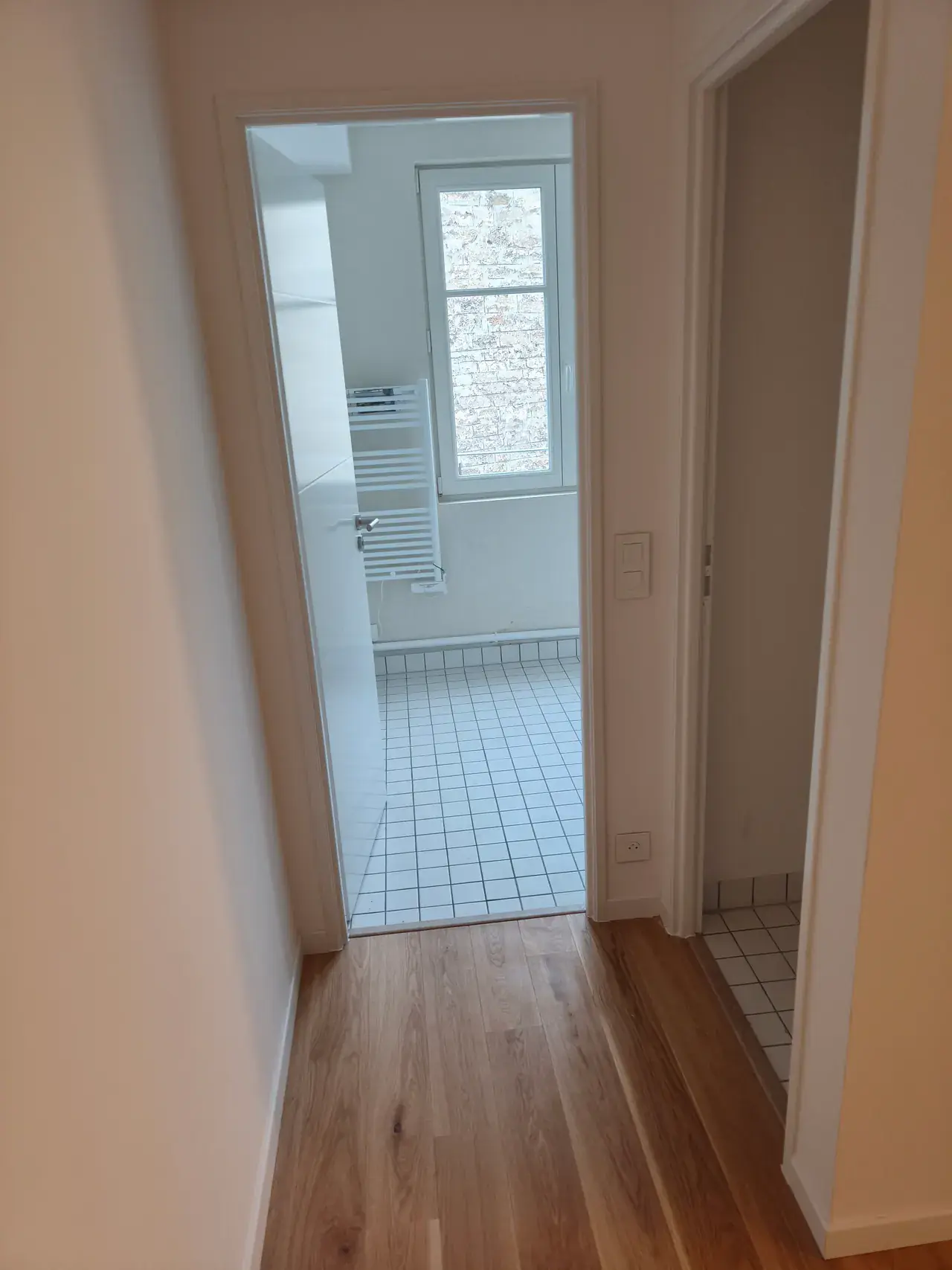 Couloir en parquet clair ouvrant sur une salle d’eau carrelée