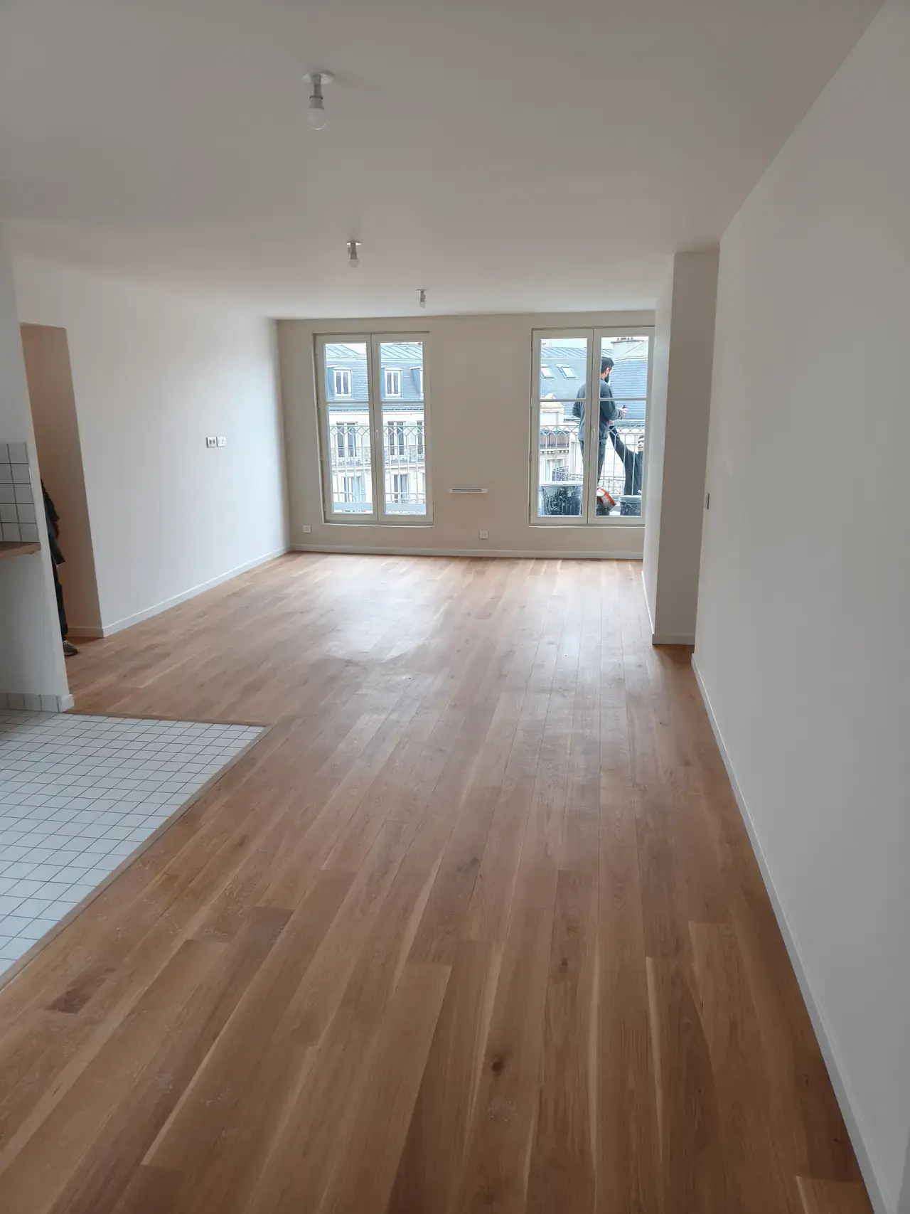 Pièce de vie livrée avec parquet chêne, deux portes-fenêtres et coin cuisine carrelé