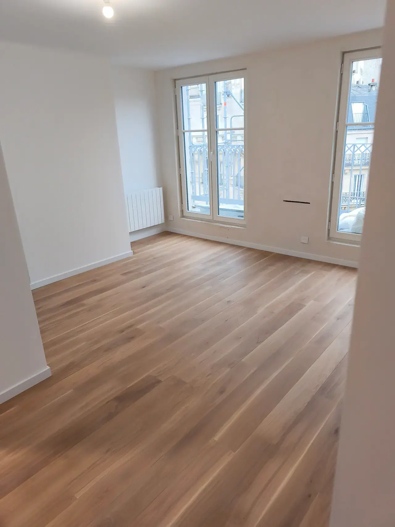 Pièce d’appartement remise en état avec parquet clair, murs blancs et portes-fenêtres