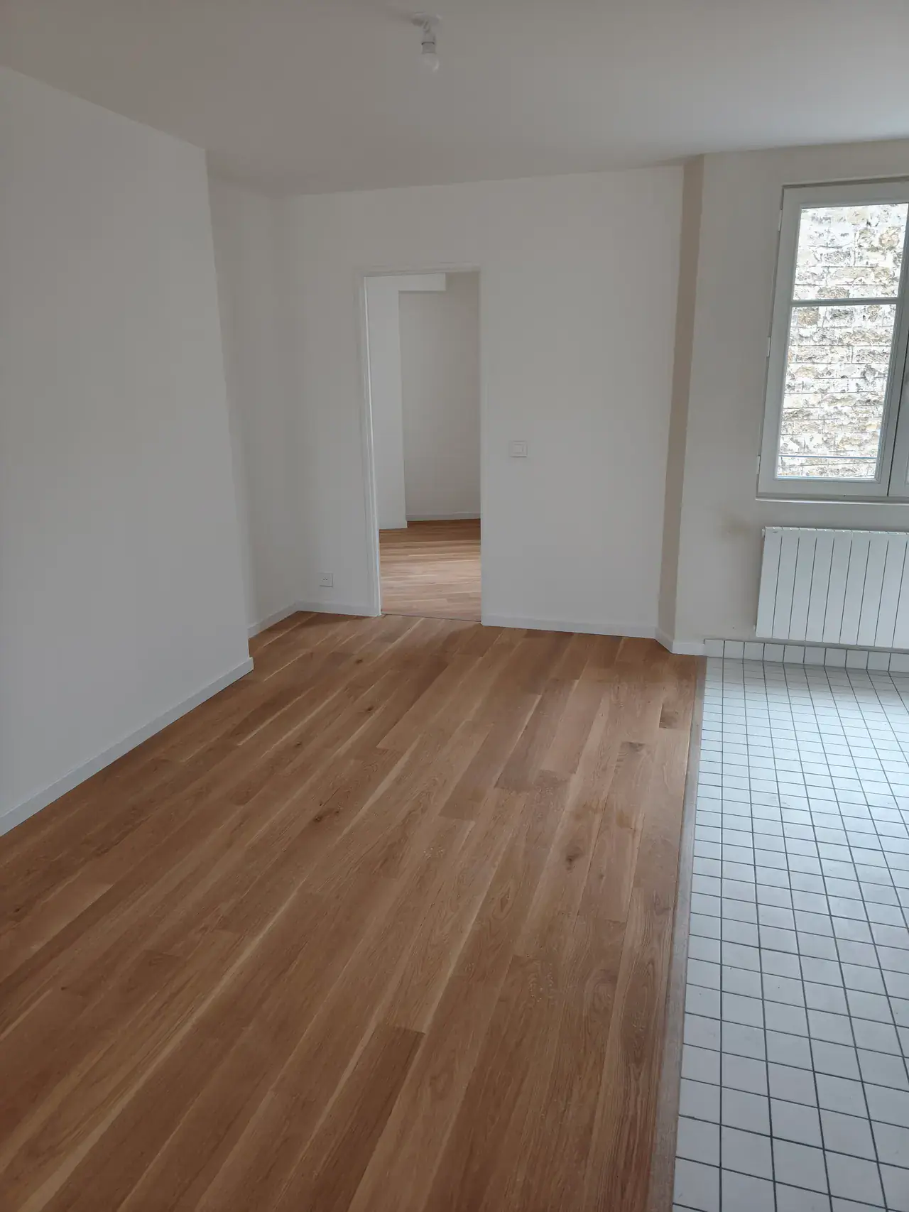 Pièce de vie livrée avec parquet clair, murs blancs et coin cuisine carrelé