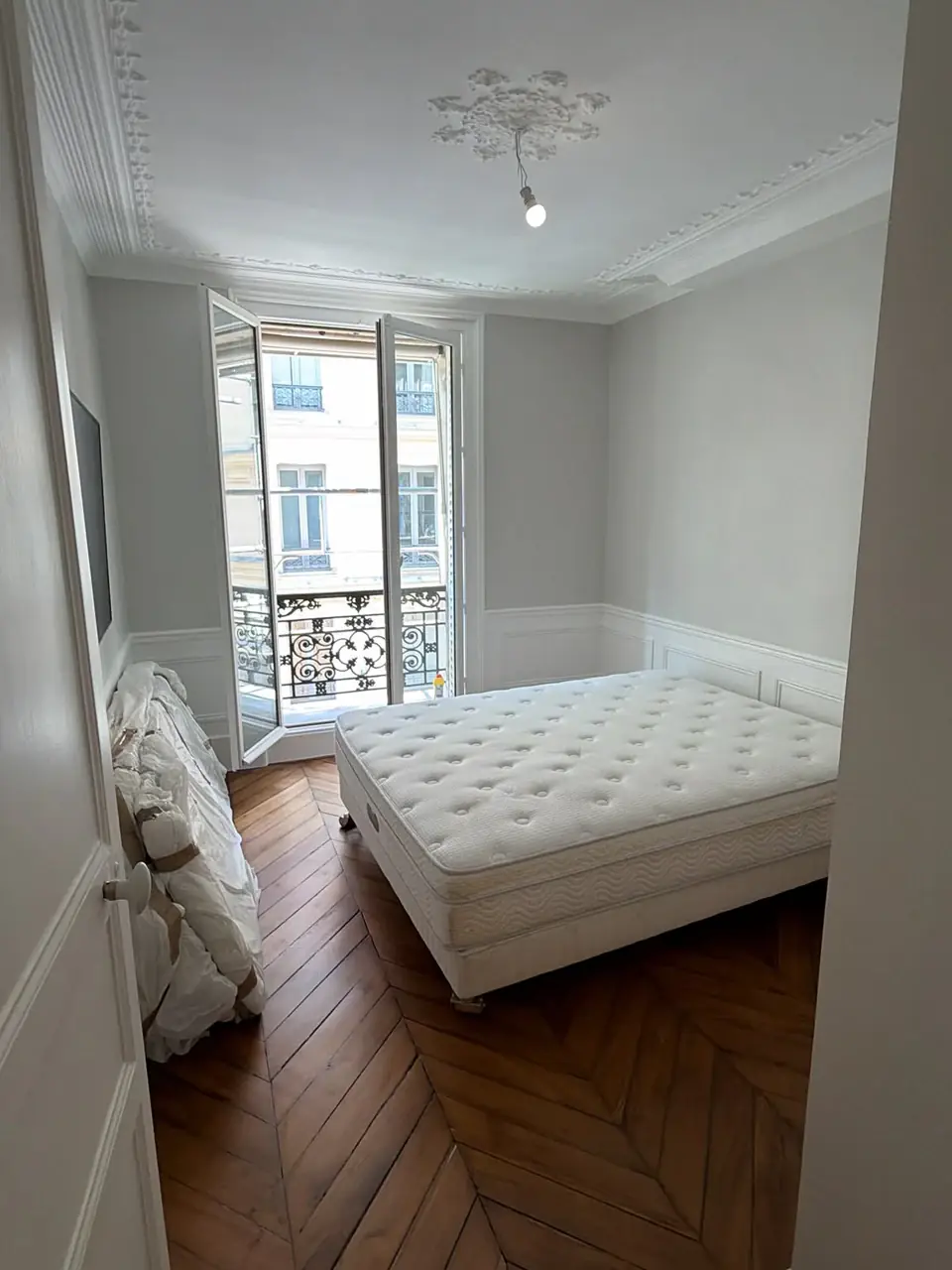 Chambre avec parquet en point de Hongrie, soubassements moulurés et porte-fenêtre sur balcon