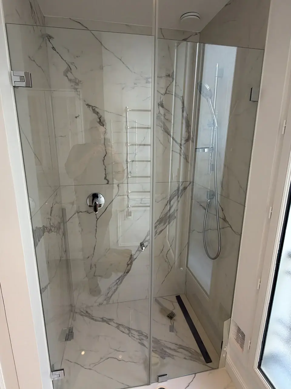 Douche à l’italienne vitrée, parois effet marbre, caniveau linéaire et robinetterie chromée