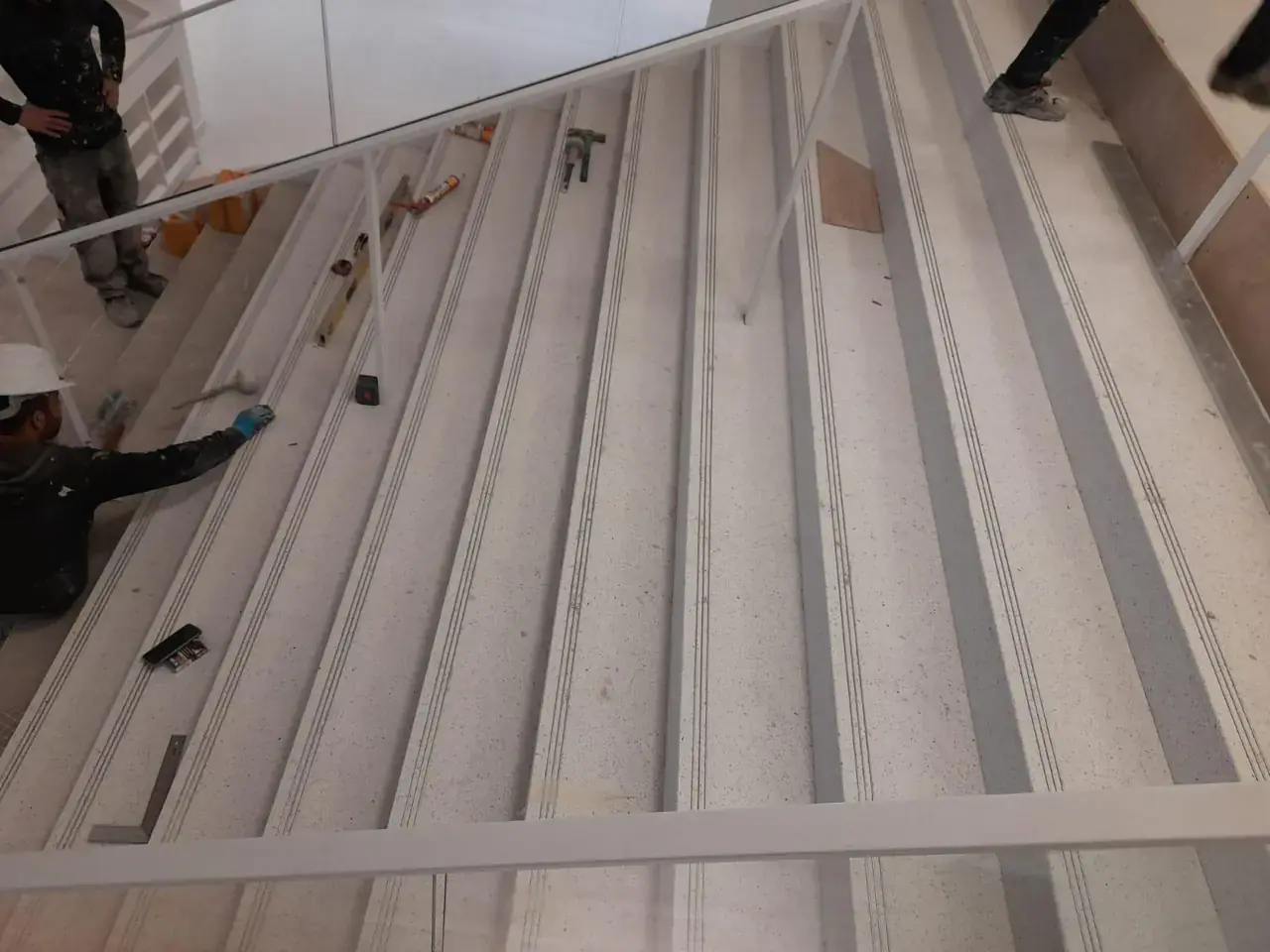 Pose des marches en terrazzo clair avec bandes antidérapantes sur un escalier d’établissement