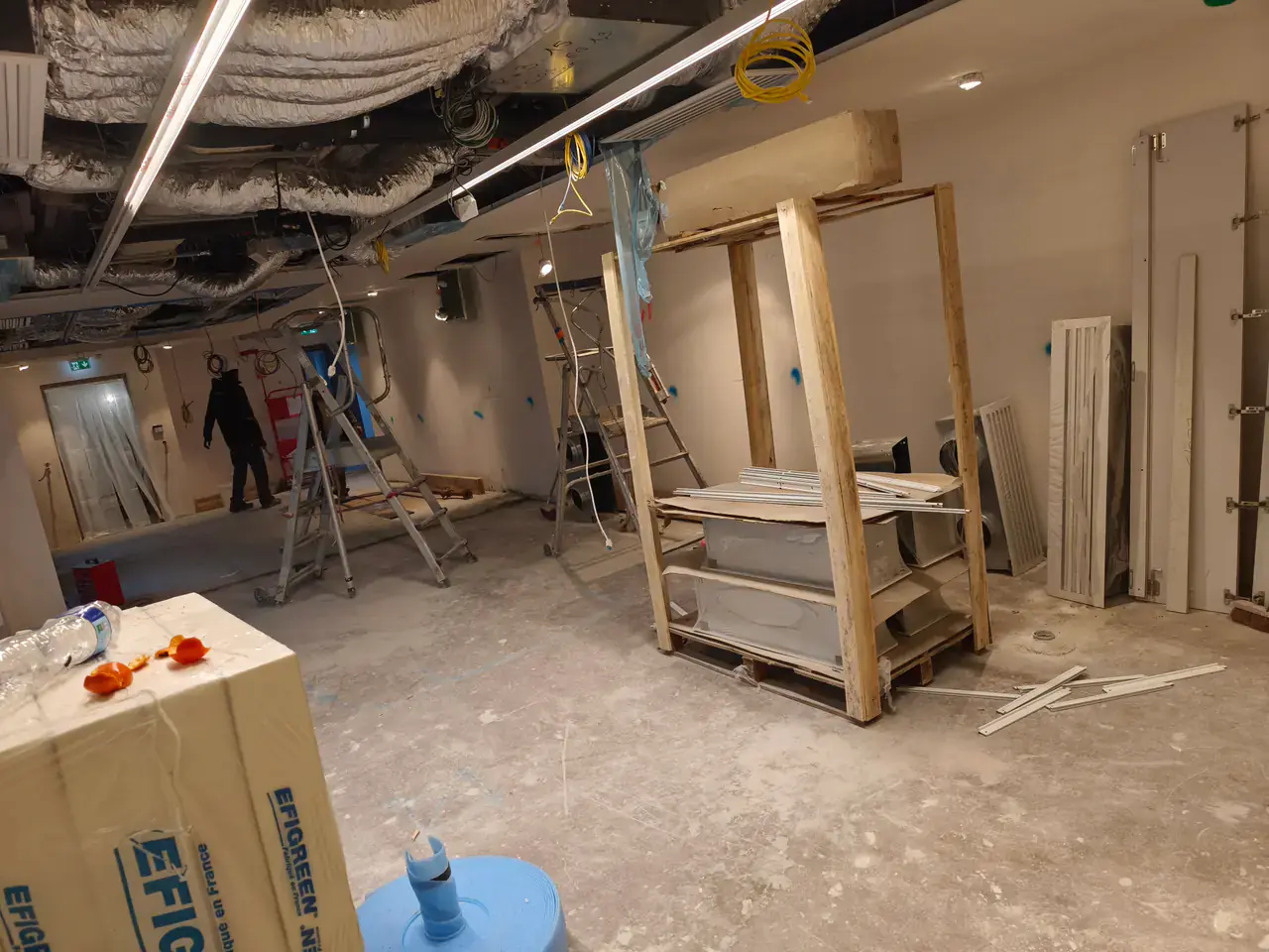 Plateau professionnel avec plafond déposé, gaines de ventilation apparentes et compagnons au travail