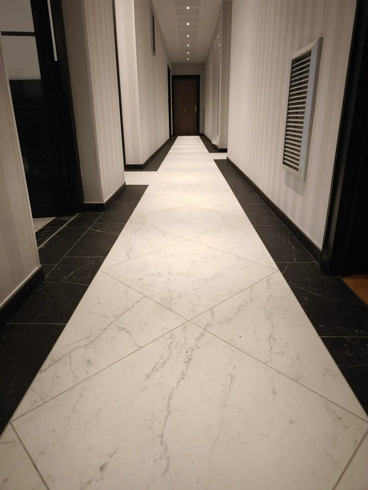 Couloir de résidence avec sol clair bordé de noir et portes sombres
