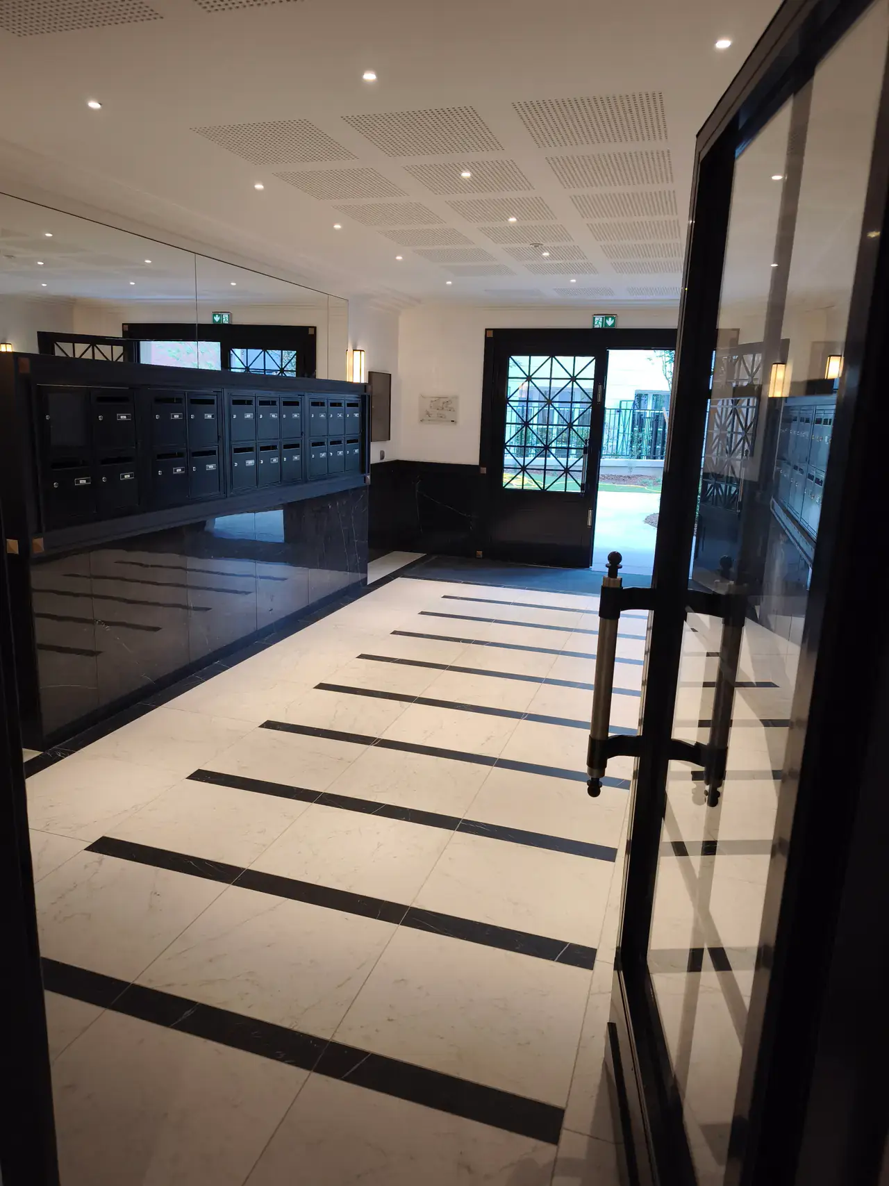 Grand hall de résidence livré avec sol clair bordé de noir et portes vitrées