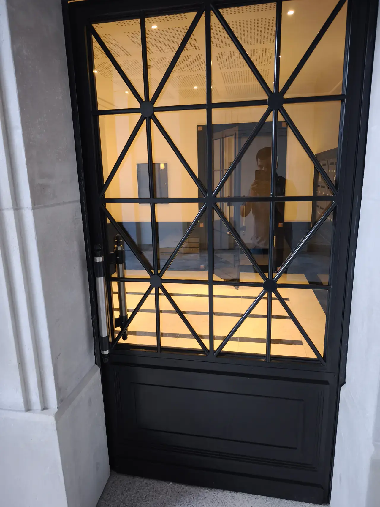 Porte vitrée noire à motifs géométriques dans le hall de la résidence