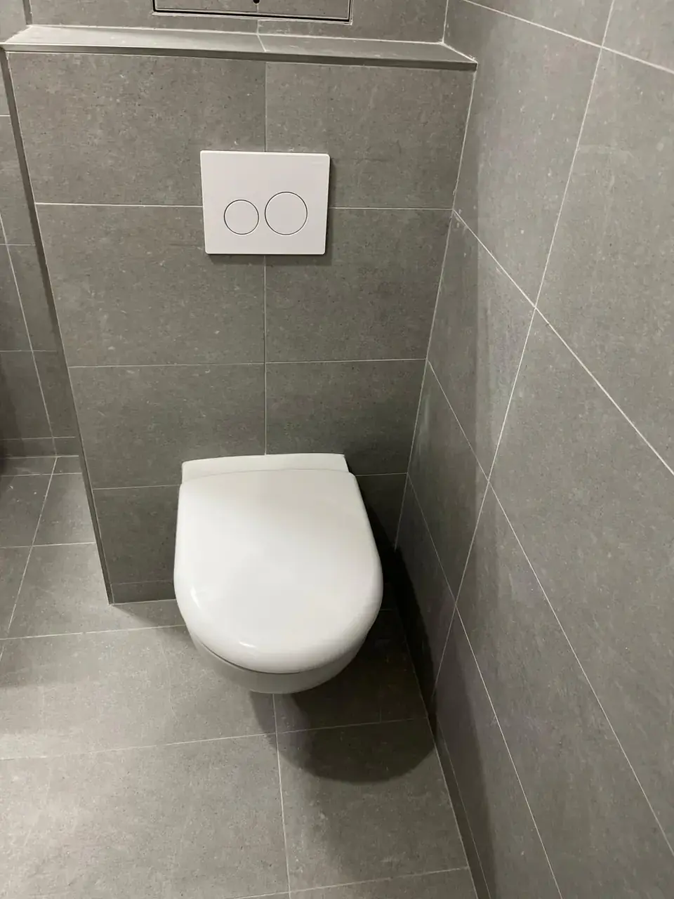 WC suspendu avec bâti habillé de carrelage gris et plaque de commande blanche