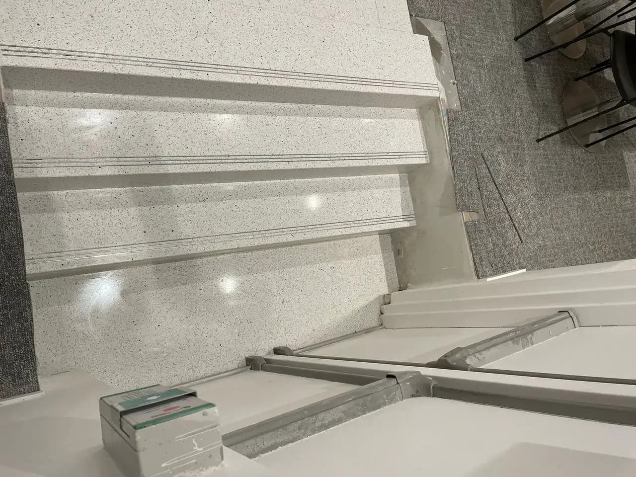 Escalier intérieur en terrazzo clair avec nez de marche rainurés, bordé de moquette