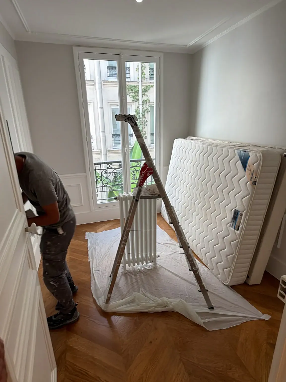 Peintre reprenant une porte dans une chambre, avec escabeau et parquet protégé