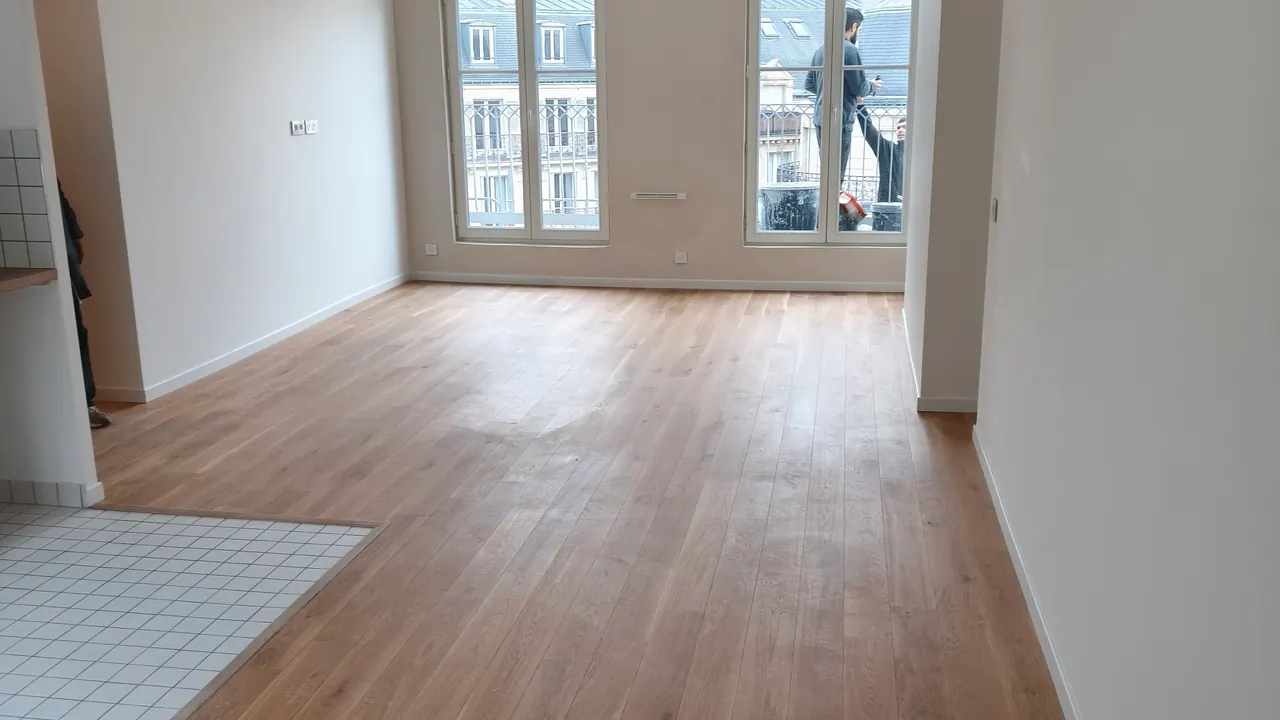 Pièce de vie avec parquet clair, murs blancs et coin cuisine carrelé