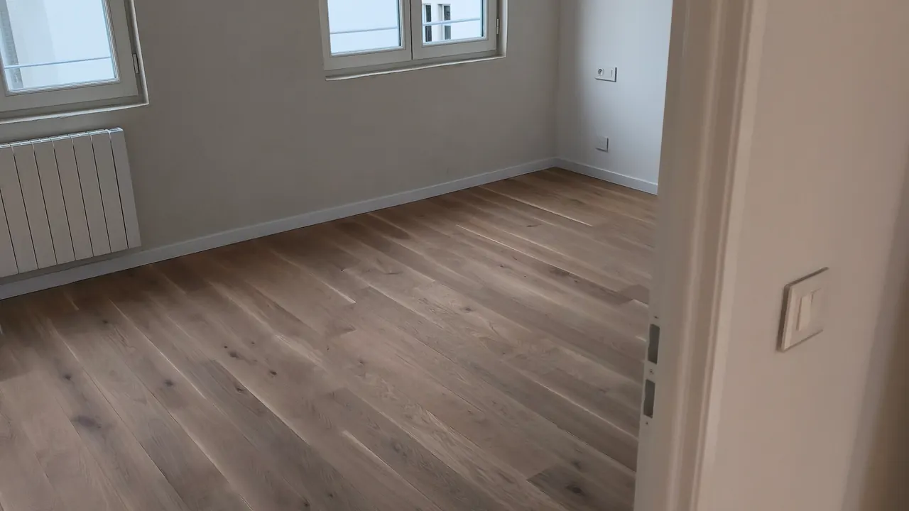 Chambre rénovée avec parquet clair, deux fenêtres et murs repeints en blanc