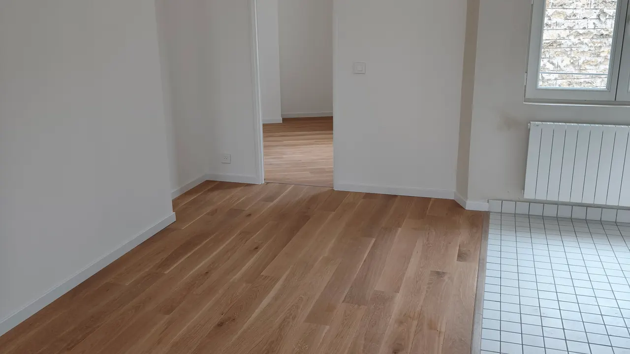 Séjour rénové avec parquet clair, murs blancs et sol carrelé dans le coin cuisine