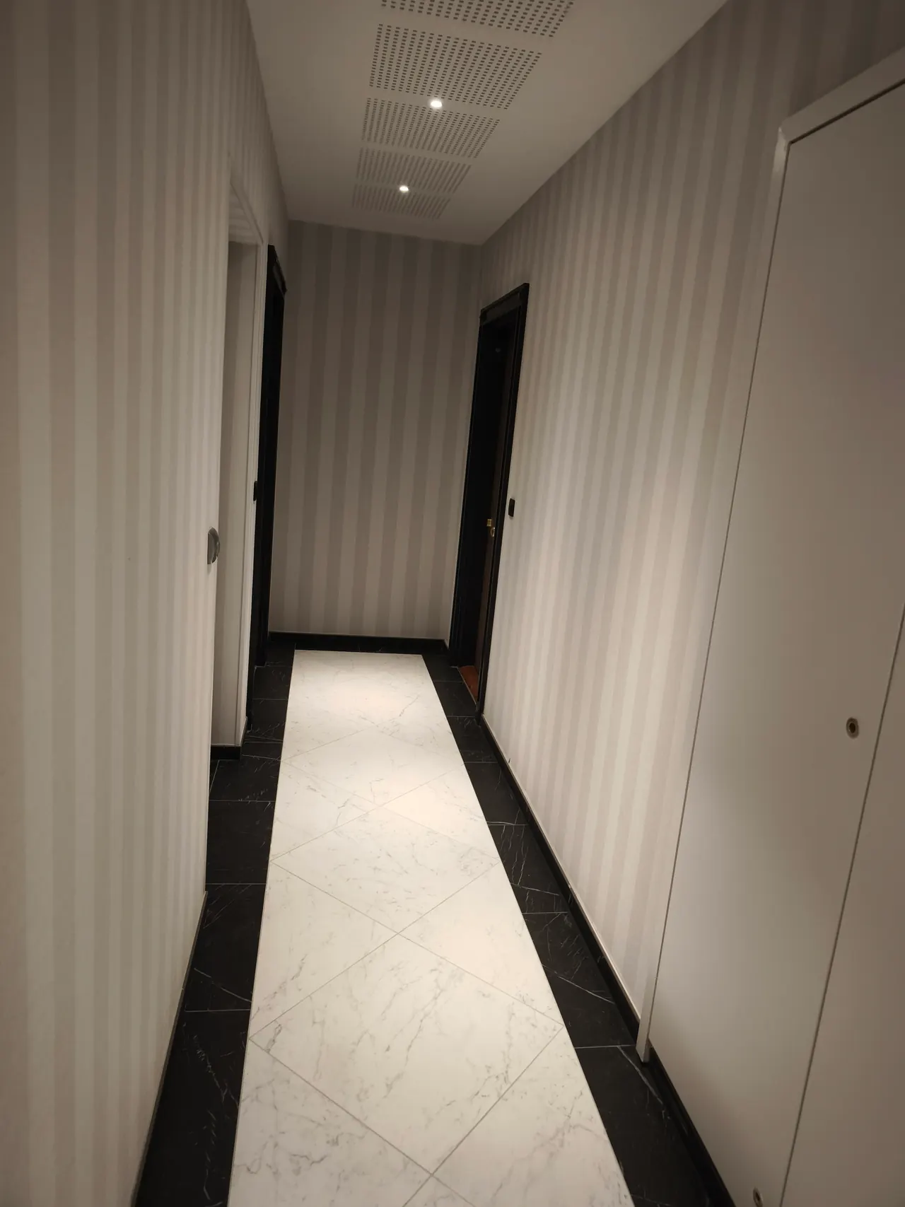 Couloir de résidence avec portes palières claires, sol bordé de noir et éclairage encastré