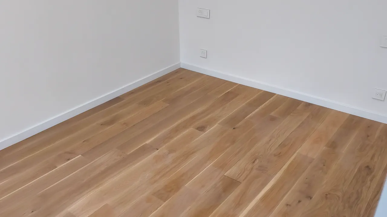 Angle de pièce avec murs blancs, plinthes claires et parquet posé